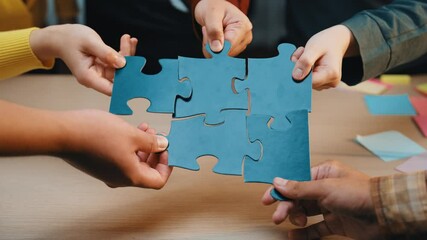 A close-up of hands from diverse business professionals working together with colorful puzzle pieces during a collaborative meeting in an office. SACTR - Powered by Adobe