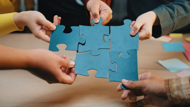 A close-up of hands from diverse business professionals working together with colorful puzzle pieces during a collaborative meeting in an office. SACTR