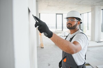 Professional indian worker plastering wall with putty knife indoors.