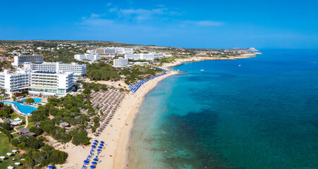 Aerial view of Ayia Napa, Cyprus, showing Nissi and Landa Beaches, turquoise waters, luxury resorts, blue umbrellas, and people enjoying the sea.