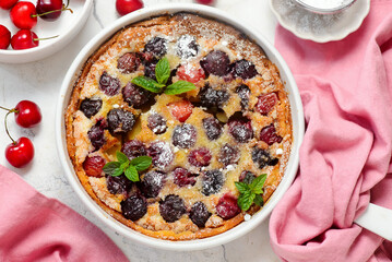Cherry clafoutis in a white pan sprinkled with powdered sugar
