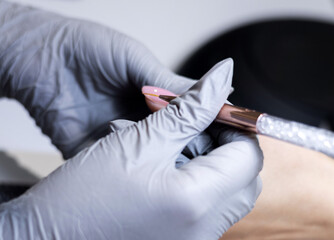 master applying gel polish on women nails in beauty salon. manicurist is polishing with file drill...
