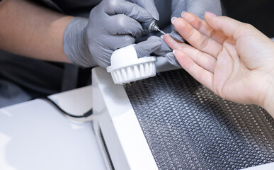 master applying gel polish on women nails in beauty salon. manicurist is polishing with file drill...