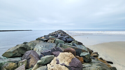 Narrow strip of green and brown rocks stretching into Pacific ocean at Point Medanos Jetty separating South Mission beach from entrance channel to the bay area, San Diego, California
