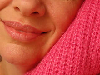 Closeup of happy woman leaning her face on pink cozy sweater. Woman enjoying warm and cozy winter clothes. 