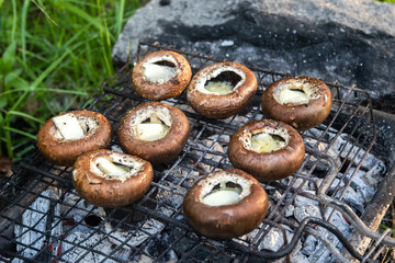 Agaricus bisporus mushrooms stuffed with butter on the grill. Picnic in nature.