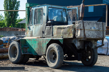 A worn-out forklift is resting on the dirt at a construction site surrounded by wooden logs and industrial equipment