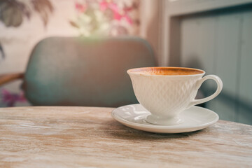 Elegant white coffee cup on wooden table with soft sunlight and blurred background in cozy cafe setting
