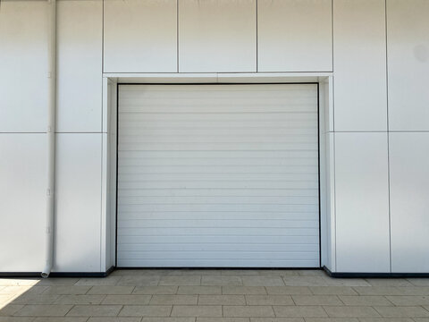 Closed automatic white metal roller shutter doors. Fragment of modern urban building,  front view. There may be garage, parking lot, storage room or store behind closed door
