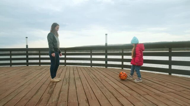 Mother and daughter at the pier near the water having fun. Mom with little girl playing a ball