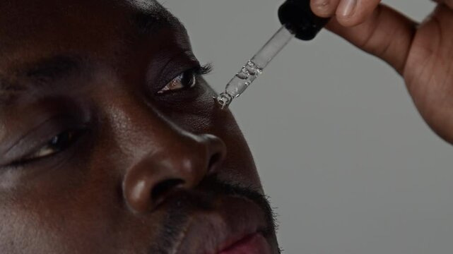 Close up shot of young Black man applying transparent moisturizing serum to his face during personal skincare routine