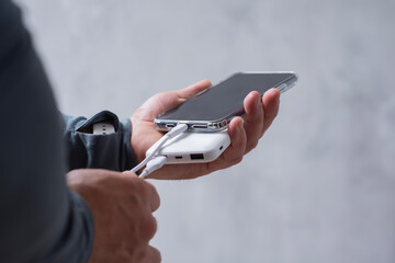 Close-up of a man holding a power bank and charging a smartphone. Portable charger for phone and gadgets.