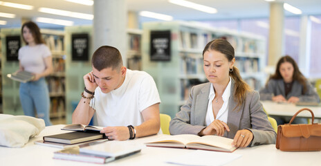 Girl and guy are sitting at table in library - reading books, preparing for exams at the university