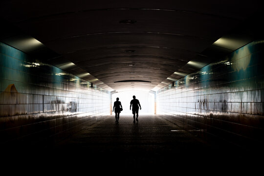Silhouettes walking toward the light in an urban tunnel
