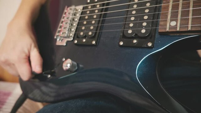 Female musician in casual clothes on bedroom playing and tuning electric guitar, while enjoying free time in domestic room.
