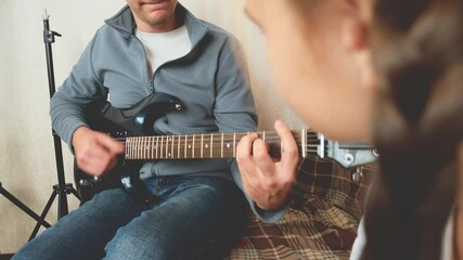 Father learning his daughter playing electric guitar in living room. Close up - Powered by Adobe