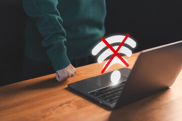 User using a laptop to connect to wifi with a crossed-out Wi-Fi symbol, representing internet disconnection and network failure stress. Concept of frustrated user waiting for connect to wifi.