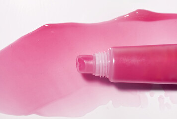 Lip gloss or tint or lip balm pink colored smudge and plastic tube sample on isolated gray...