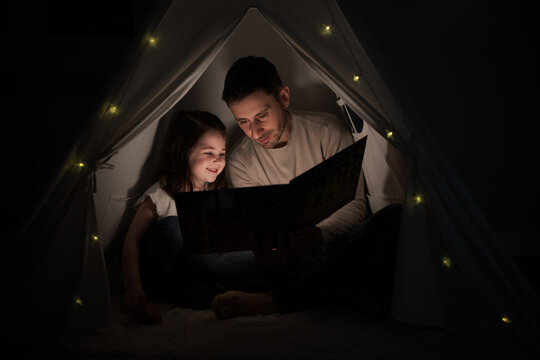 Father reading a bedtime story to his daughter in a blanket fort