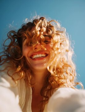 Joyful Woman with Windblown Curly Hair Against Blue Sky