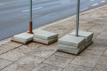 Two large, concrete block bases supporting a metal pole, likely for a sign or barrier, on a paved...