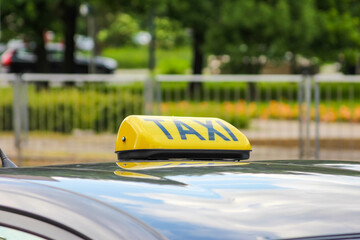 The yellow taxi sign on the roof of a parked car, with a blurred urban background on a sunny day.