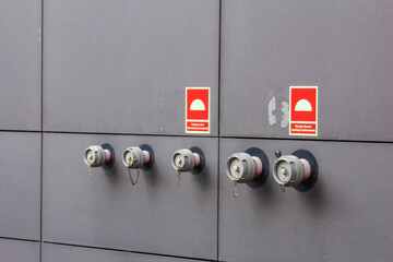 A row of silver fire hydrants or alarm connections mounted on a grey building wall, with red...