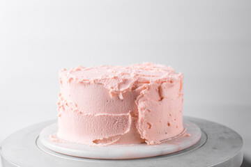 Cake being covered in pink buttercream frosting, cake being covered in pink american buttercream, process of decorating a cake