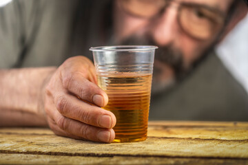 Hands of lonely drunk man with dirty nails and raised cuticles, holding glass of whiskey on blurred background