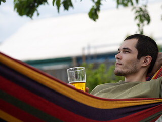 A man with a glass of beer lies in a hammock. Relaxing in the garden