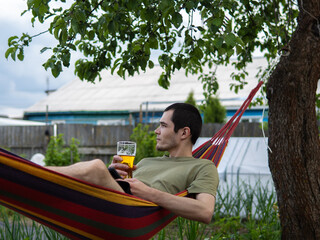 Young man with beer glass lying on hammock in garden