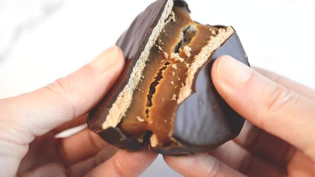 Female hands breaking a chocolate alfajor filled with dulce de leche.