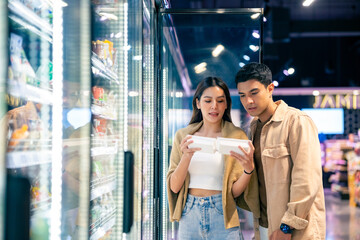 Happy Asian family couple shopping buying organic frozen food at supermarket. Man and woman...