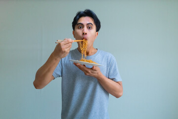 Happy young Asian man enjoying a plate of noodles with a cheerful expression, isolated on a clear background, perfect for food, lifestyle, or Southeast Asian culture themes