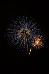 A pair of overlapping firework burst on a black sky.  The smaller in golden and red.   The larger is blue with white sparkles