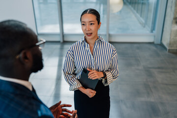 Businesswoman holding tablet talking to businessman in office hallway