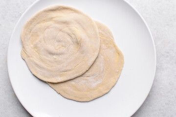 Overhead view of rolled paratha dough, top view of flaky flatbread dough, process of making paratha