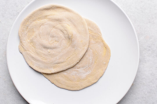 Overhead view of rolled paratha dough, top view of flaky flatbread dough, process of making paratha