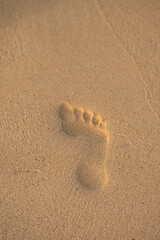A foot print is in the sand. The sand is brown and the foot print is white. The image has a calm and peaceful mood