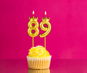 Birthday celebration with number 89 candle - Yellow cupcake on a pink background