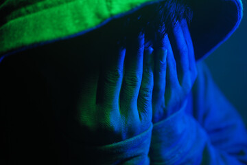Person hiding face in dim light with colored lights