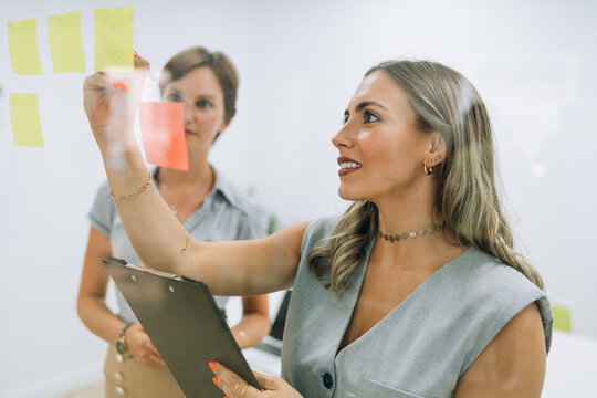 Businesswomen planning strategy using sticky notes on glass wall 
