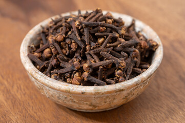 Stone bowl with dried clove buds, used for cooking and traditional medicine, close-up, spices collection