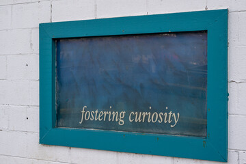 A green wooden frame around a black chalkboard. The inspirational phrase fostering curiosity is...