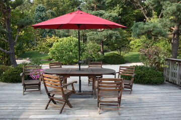 Obraz premium Wooden patio with red umbrella and empty chairs in a peaceful garden setting