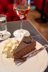 Piece of famous Sachertorte chocolate cake with apricot jam of Austrian origin served with whipped cream in old classic cafe-restaurant in Vienna