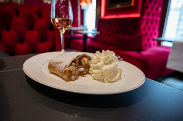 Austrian desserts, piece of apple strudel with whipped cream served with glass of wine in traditional bakery cafe in Vienna, close up