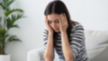 Blurred female figure sitting indoors with hands on head. Image is suitable for concepts of stress, confusion, or mental health.