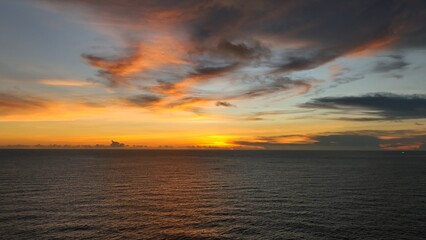 A breathtaking aerial view captures the vibrant tropical sunset, with the sky painted in warm hues of orange and pink as the sun dips below the horizon, casting a golden glow over the ocean. Thailand.