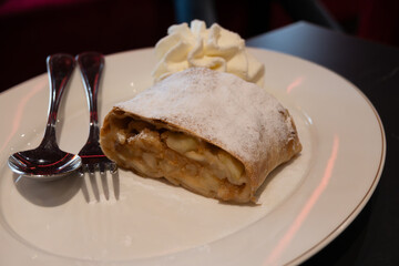 Austrian desserts, piece of apple strudel with whipped cream served in old traditional bakery cafe in Vienna, close up